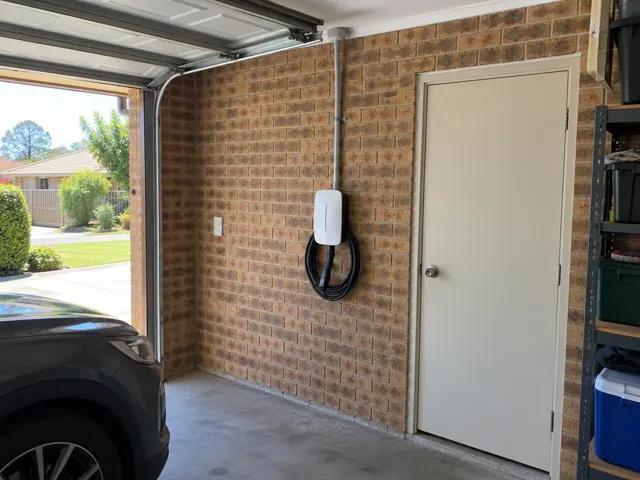 Wall-mounted EV charger on a brick garage wall beside a door in a suburban home garage in Jewells